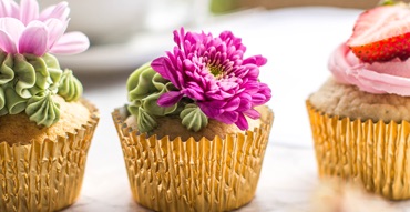 Three floral cupcakes which are decorated by fresh flowers, green cream and cutted strawbarries.