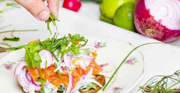 A dish of salmon salad with onion and leaves is making on a withe plate.