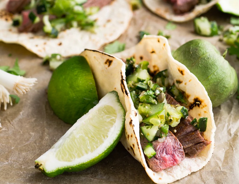 A wrap with medium well beef and vegatable an two pieces of lemon beside it.