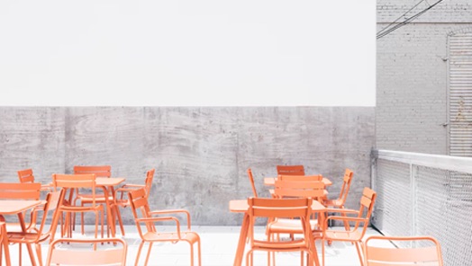 The restuarant environment, orange tables and chairs, dark gray lower half wall and barrier and light gray higher half wall.