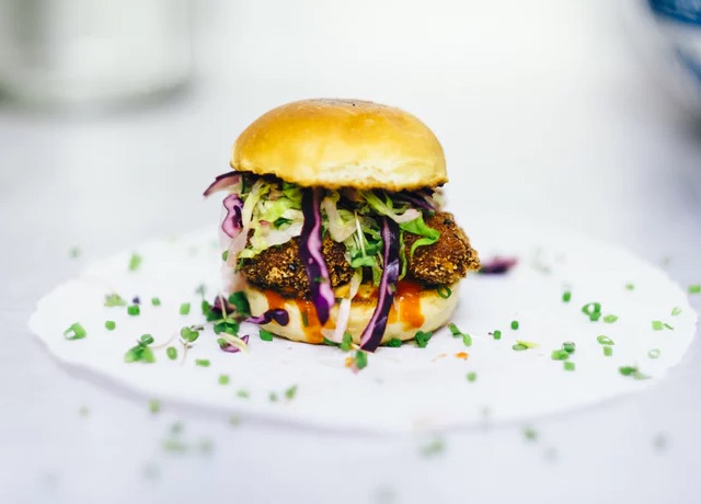 A chicken burger with green and purple cabbages.
